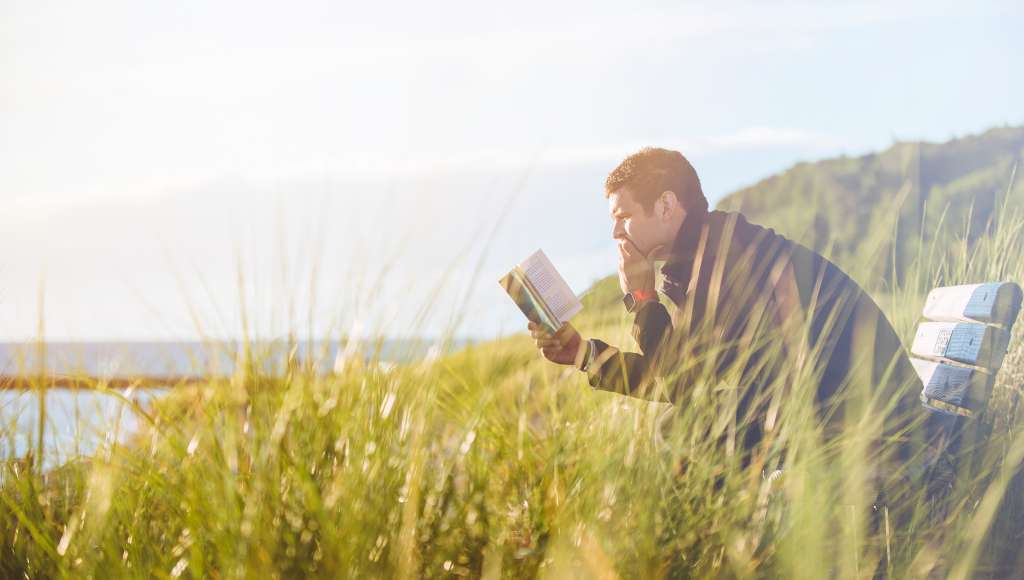 Man reading on bench by sea