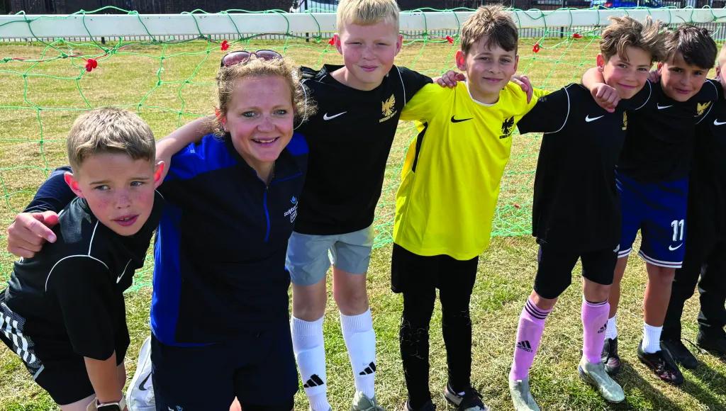 Woman and group of 5 boys pose for photo on a grass field
