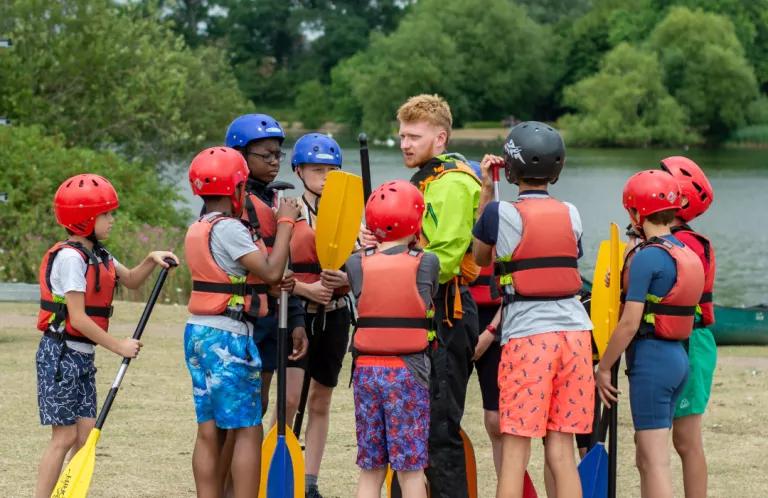 Group of young people wearing water sport equipment, standing around a group leader