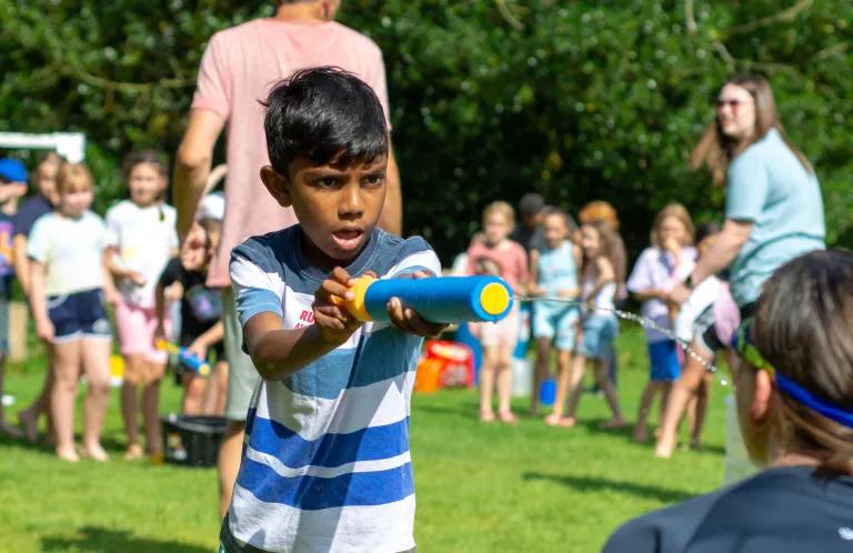 A child squirting a water pistol at a leader's face