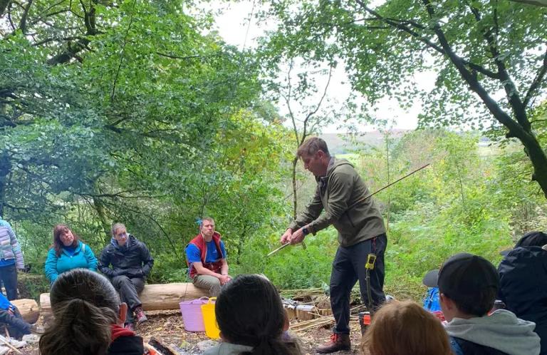 a group of young people sit around a campfire watching a leader speak