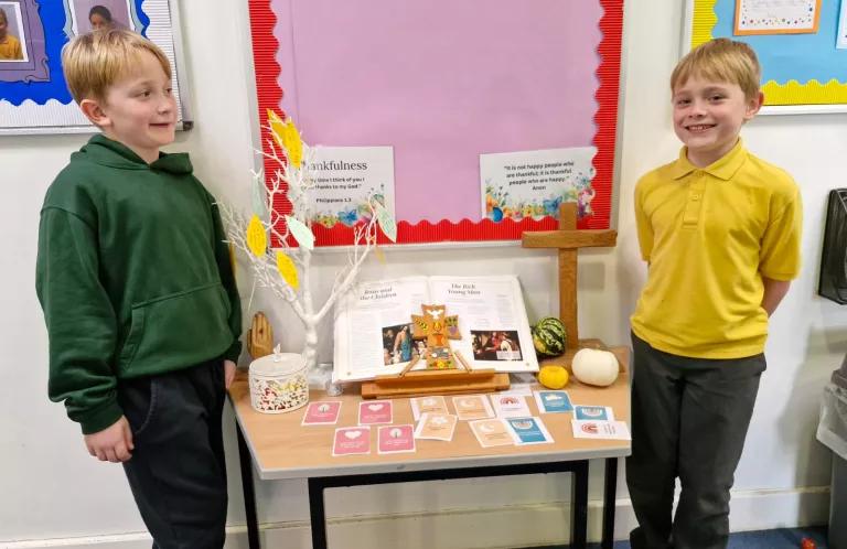Two primary age children stand next to a table covered with creative prayer resources and SU Rooted cards