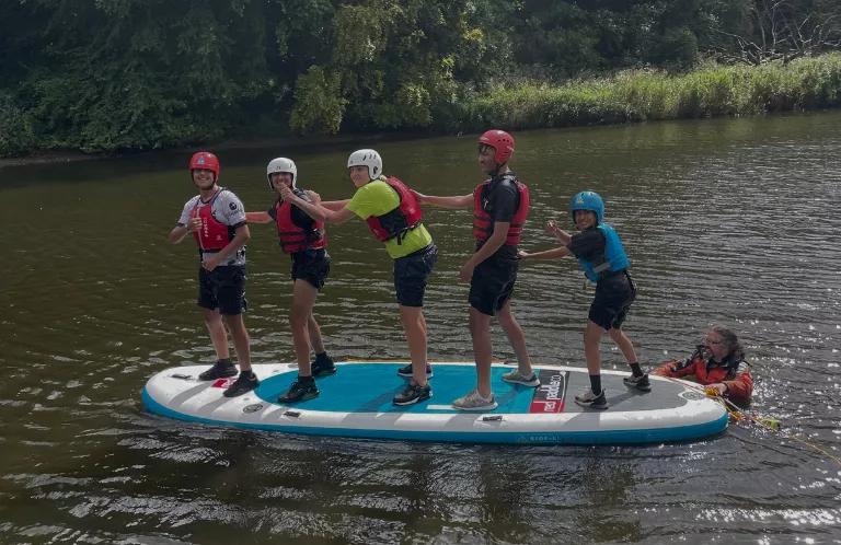 A group of five boys stand together on a paddleboard.
