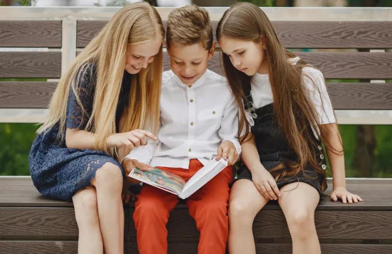 Two girls and a boy on a bench reading