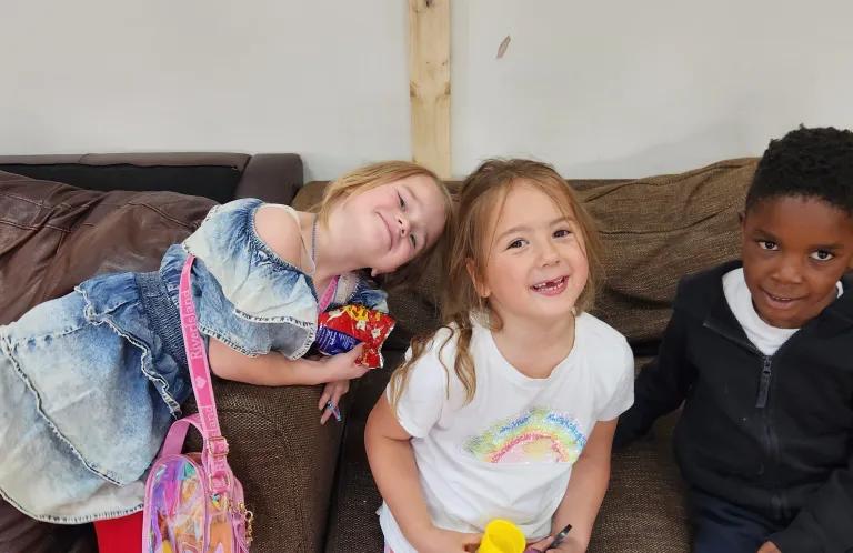 3 young children laughing on sofa